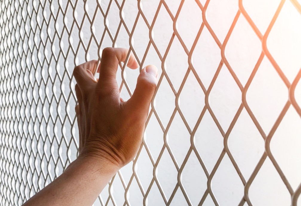 a criminal's hand gripping the fencing that keeps them inside