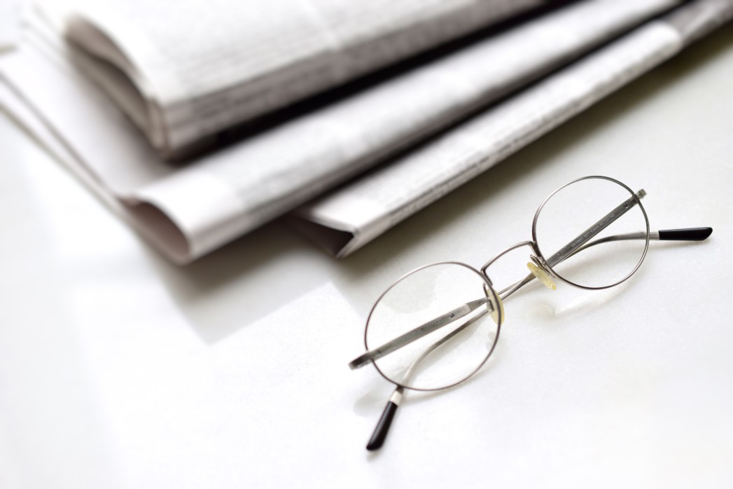 newspapers on a table with a pair of eyeglasses in front of the pile